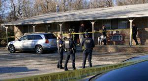 Police officers stand outside a crime scene, while other officers inspect the building